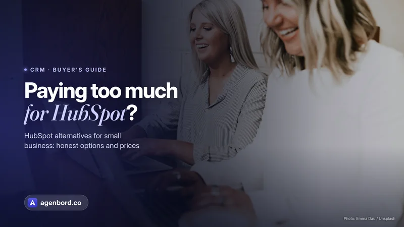 Two colleagues laughing while they work on laptops. Headline: Paying too much for HubSpot?